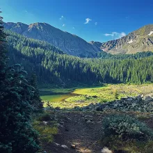 Williams Lake sits in a green alpine meadow below forested slopes and rocky peaks near Taos Ski Valley.