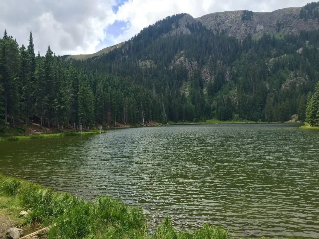 Middle Fork Lake above Red River, its forested shoreline backed by a rocky ridge in the Carson National Forest.